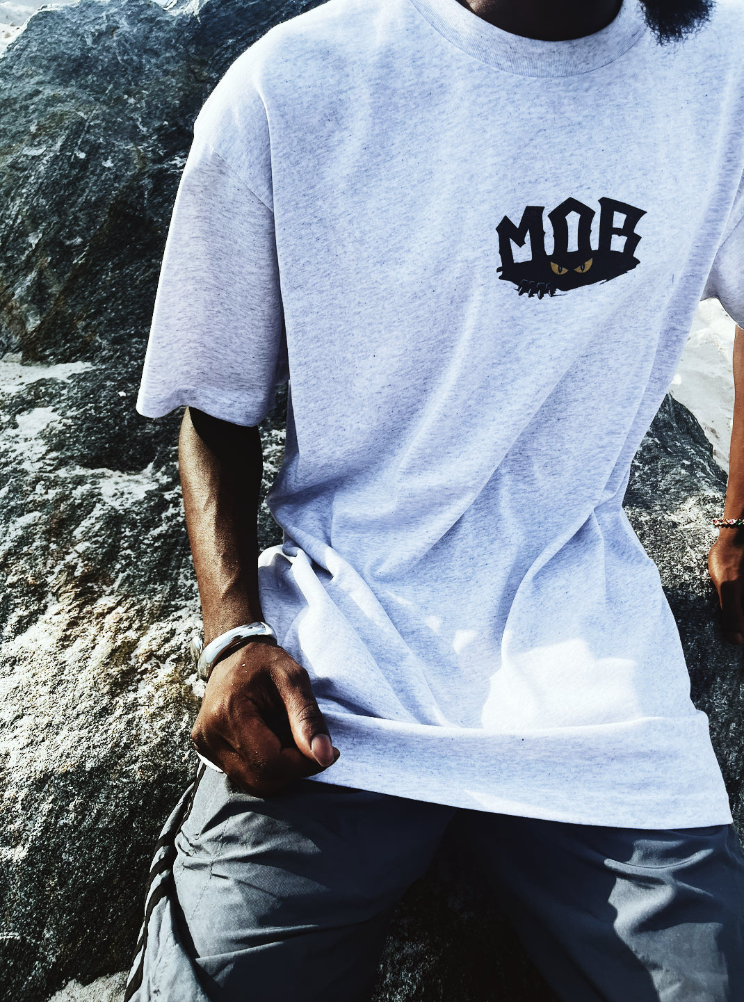 Person wearing a white t-shirt with 'MOB' logo sitting on rocks.