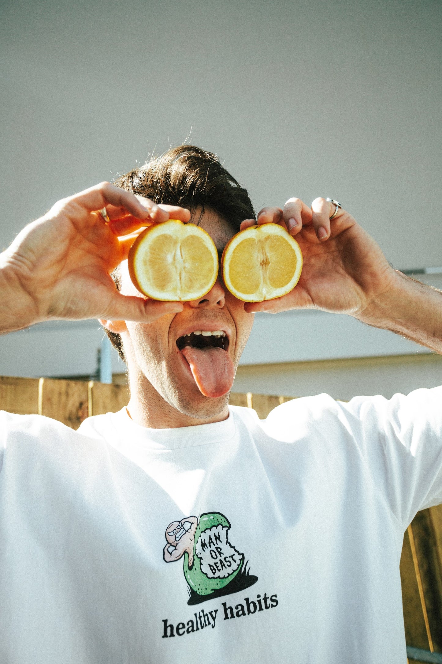Person holding lemon halves over eyes with a white t-shirt featuring a logo and text.