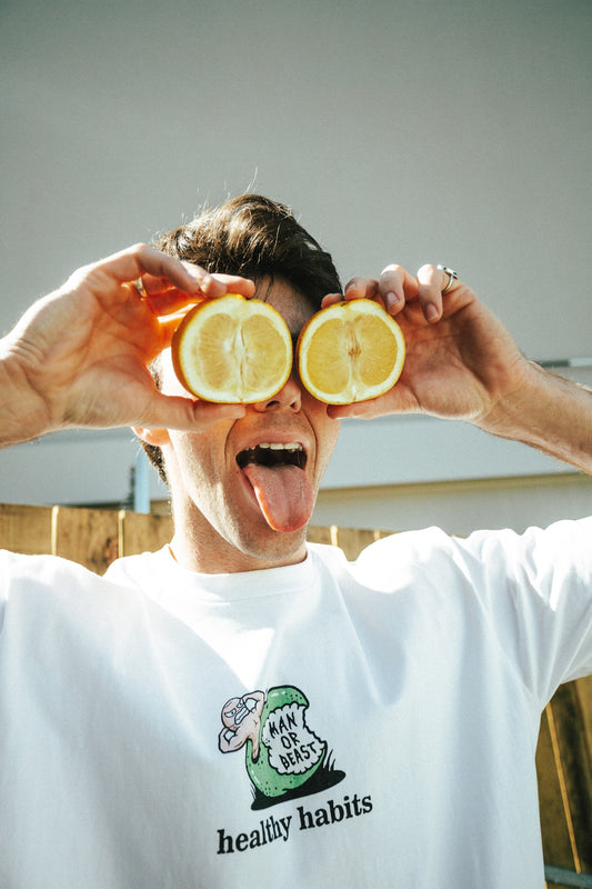 Person holding lemon halves over eyes with a white t-shirt featuring a logo and text.