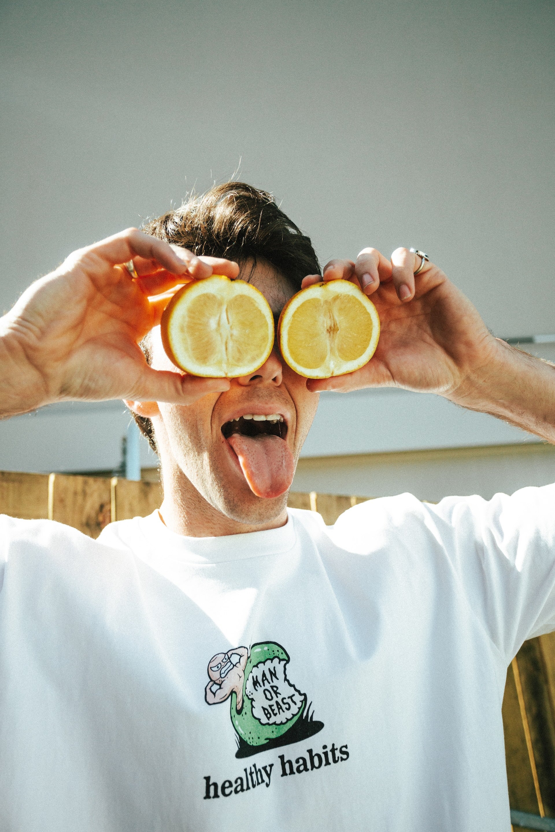 Person holding lemon halves over eyes with a white t-shirt featuring a logo and text.